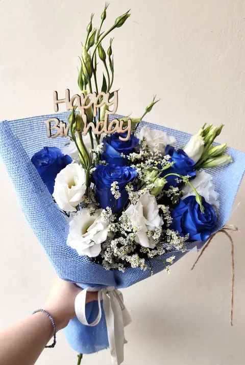 Vibrant Happy Birthday bouquet with five blue roses, lysianthus, lemonium or gypsophila, greenery, and a “Happy Birthday” mes