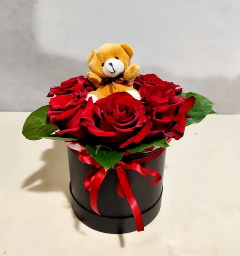 Gift arrangement with vibrant red roses and a cuddly teddy bear in a black luxury box